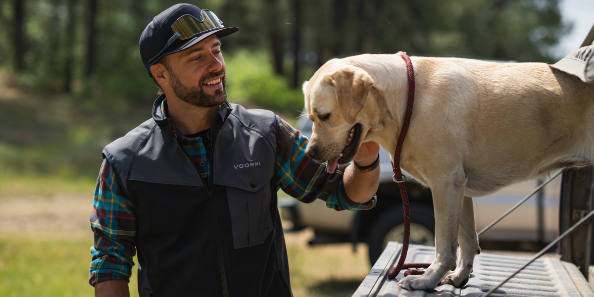 Man petting a dog on a truck bed with a forest in the background
